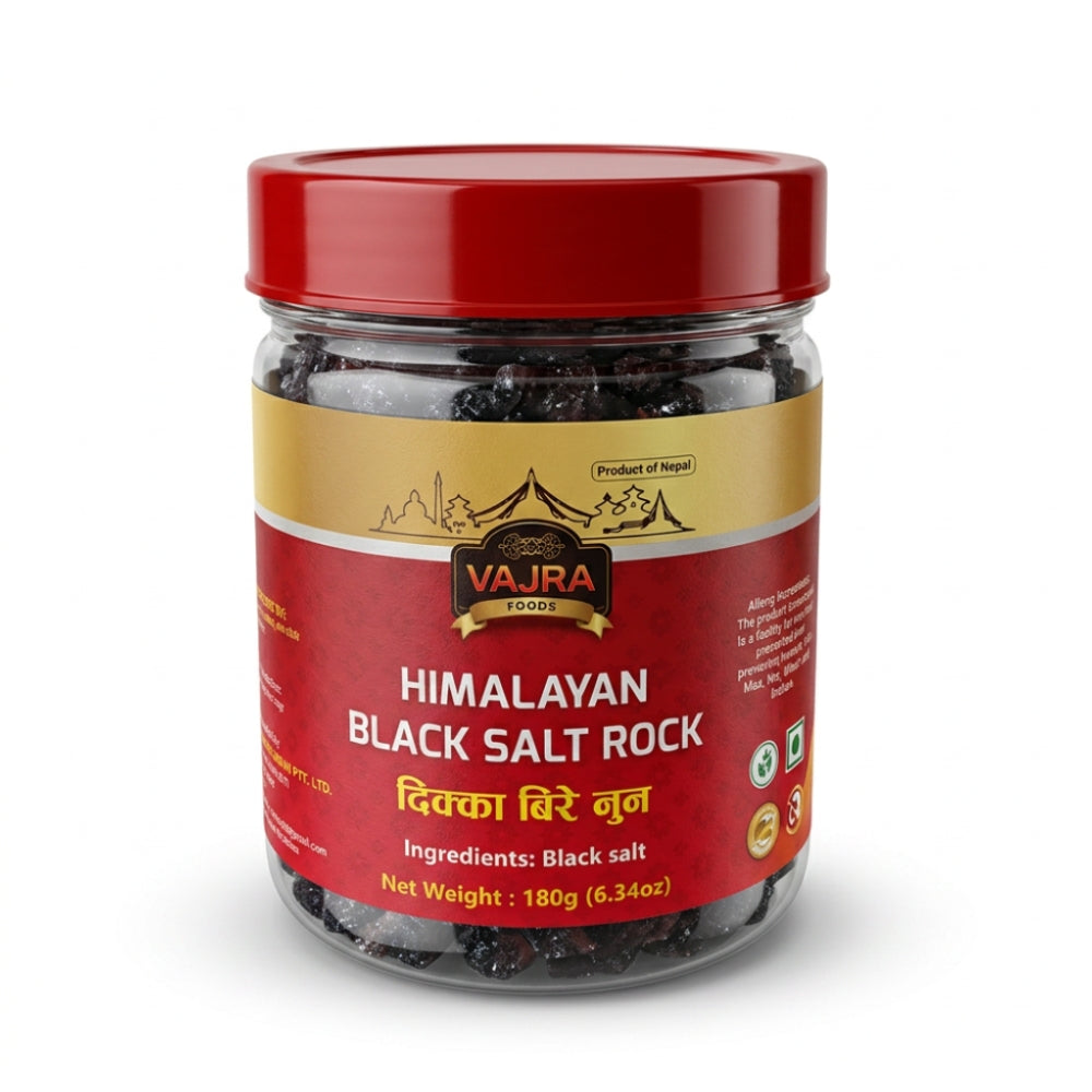 A jar of Vajra Foods Himalayan Black Salt Rock, featuring a red lid and a red and gold label, set against a plain white background.